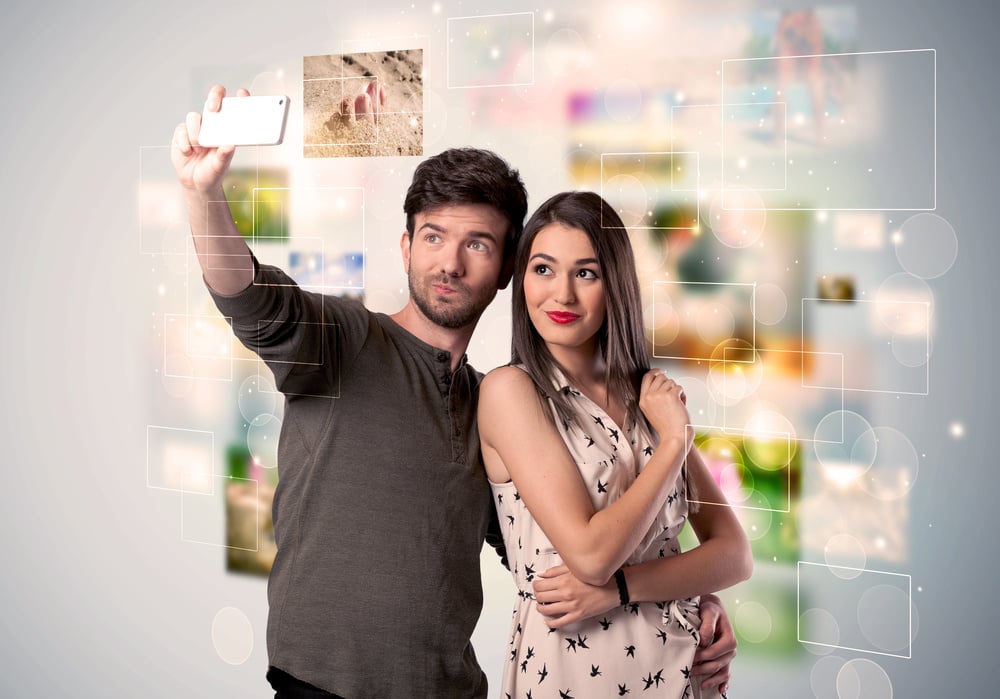 Collecting memories concept with photos in backbround and a happy young couple in love taking selfie with a mobile phone